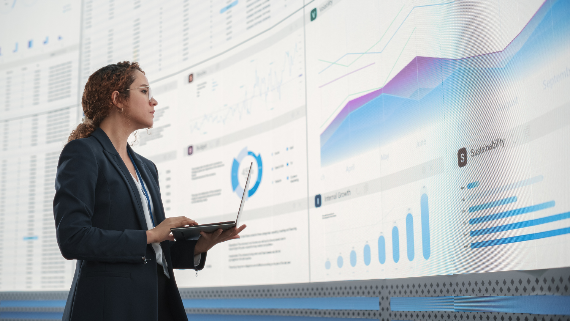 A businesswoman in a suit analyzing graphs and data on a large screen, showcasing digital transformation.