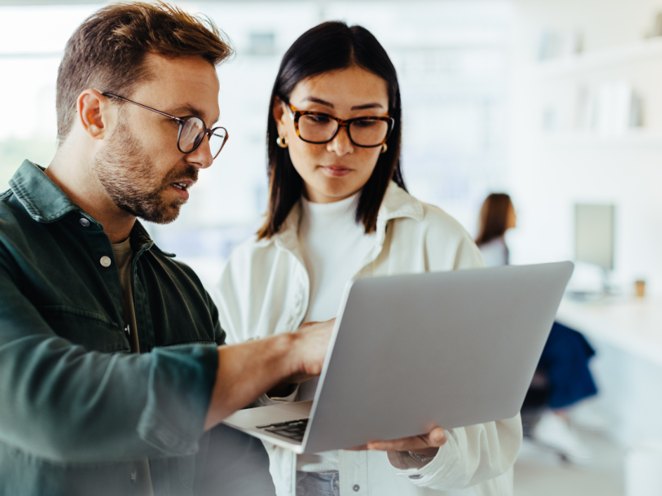 A man and woman gazing at a laptop. Reach out to DeGroote Faculty and Research team.