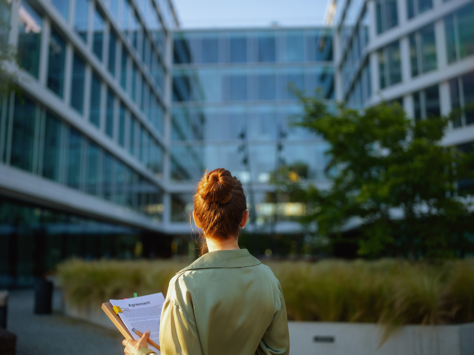 A woman standing in front of a building with a clipboard, outside of a research Center