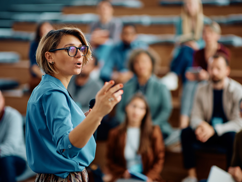 Female researcher in glasses delivering a presentation to a group of people at the DeGroote School of Business.