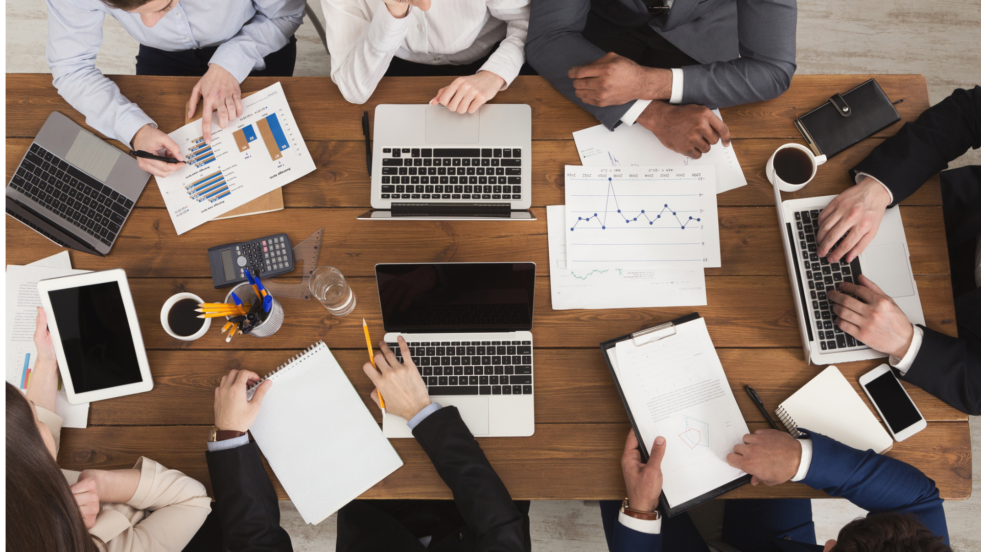 A diverse business team sitting around a table with laptops and paper.