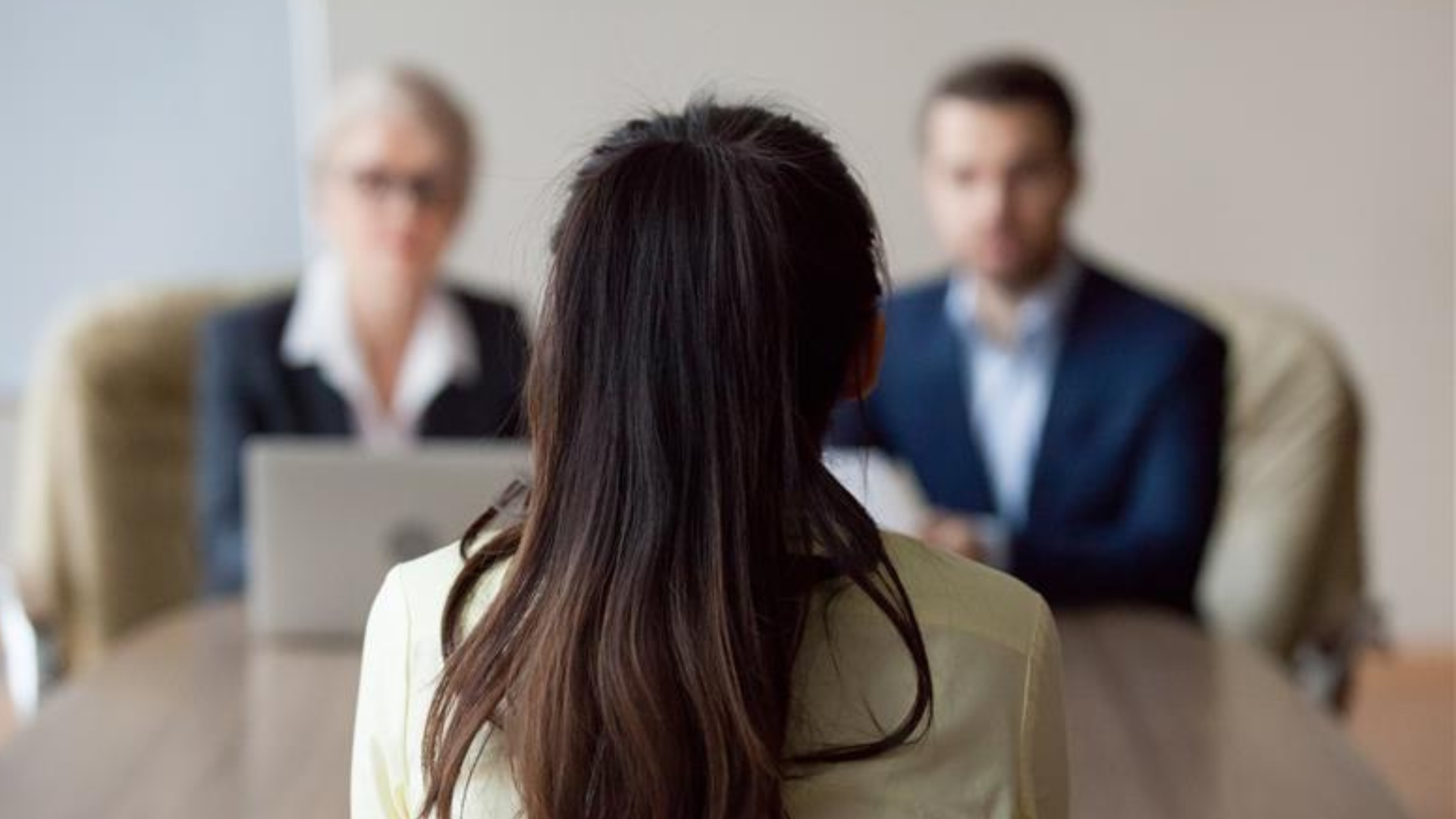 A businesswoman and businessman, both HR managers, interviewing a woman in a professional office setting.