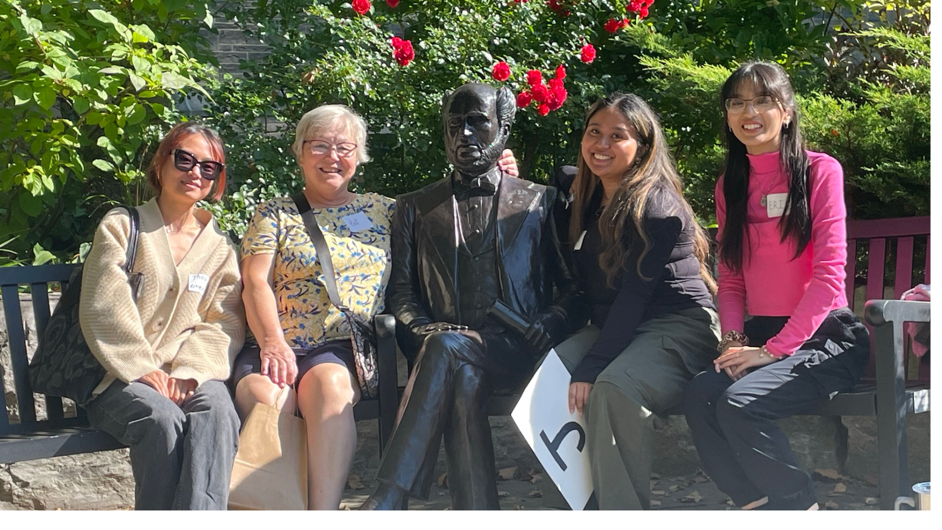Four women of varying ages and ethnicities, sit next to the the McMaster founder statue.
