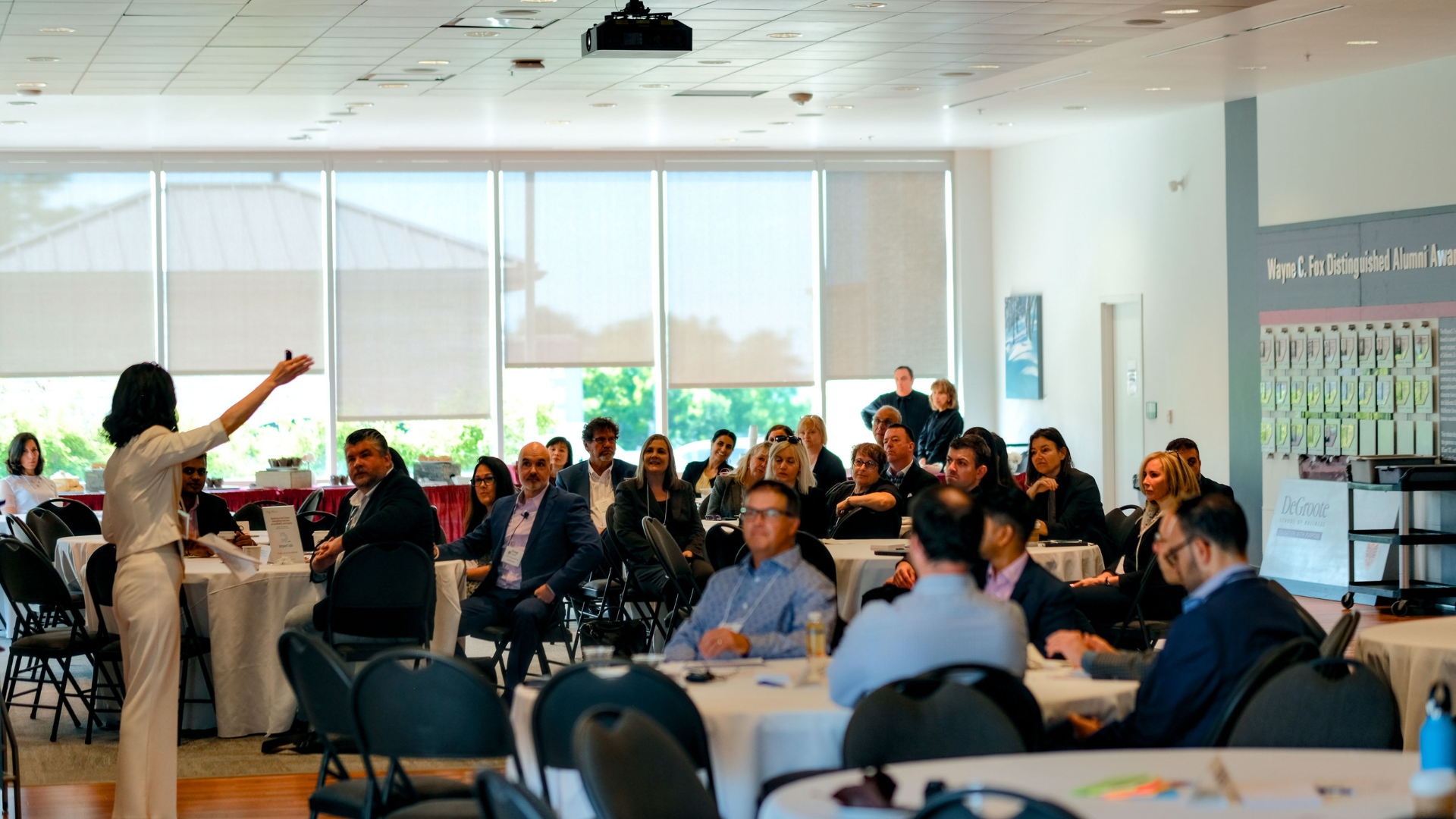A professor is gesturing and presenting to a crowd of executives.