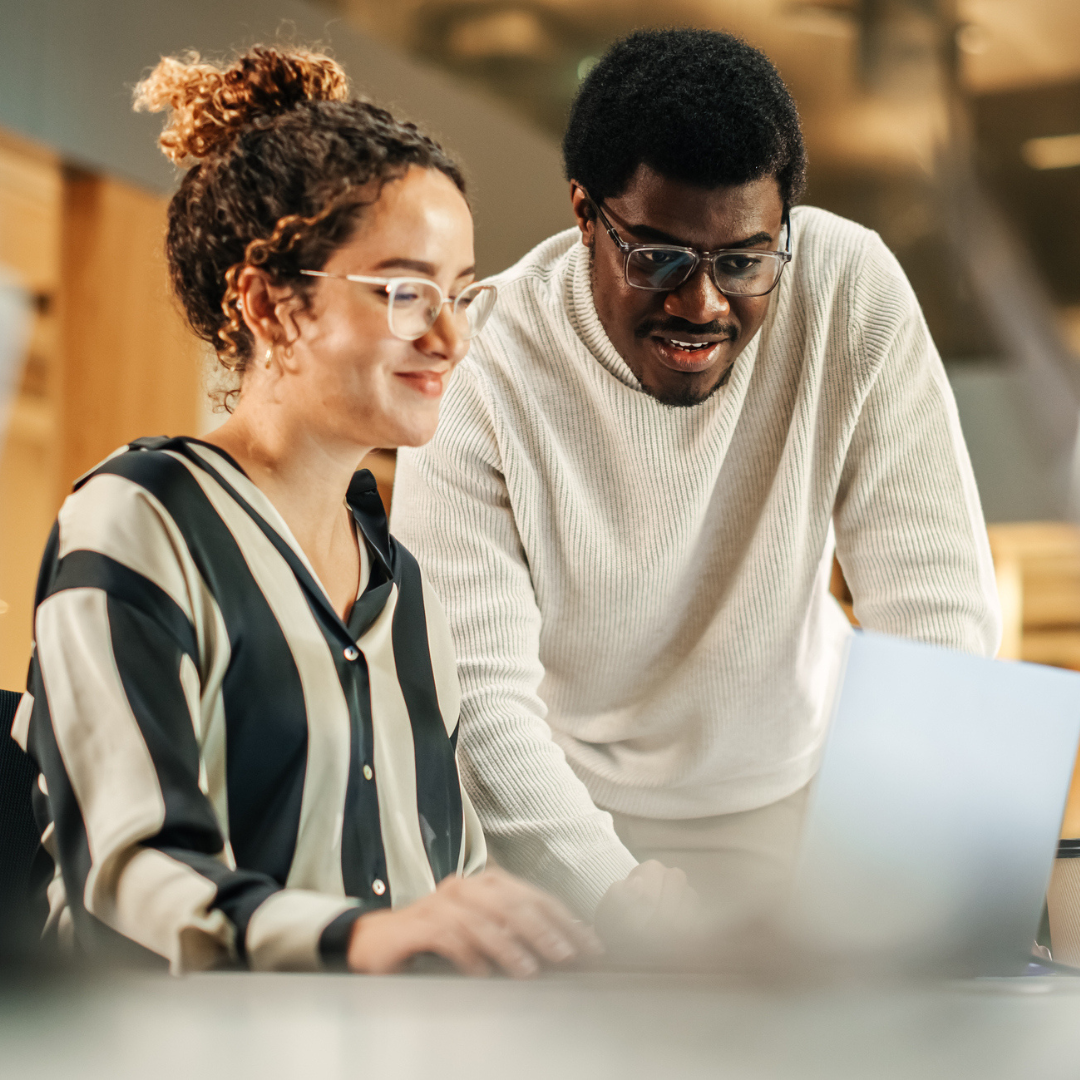 Two diverse researchers collaborate while looking at a laptop.
