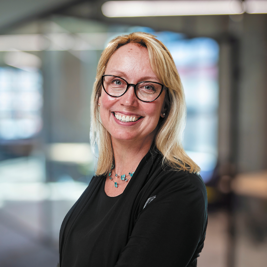 Headshot of Milena Head, a smiling woman wearing glasses and a black jacket and shirt.