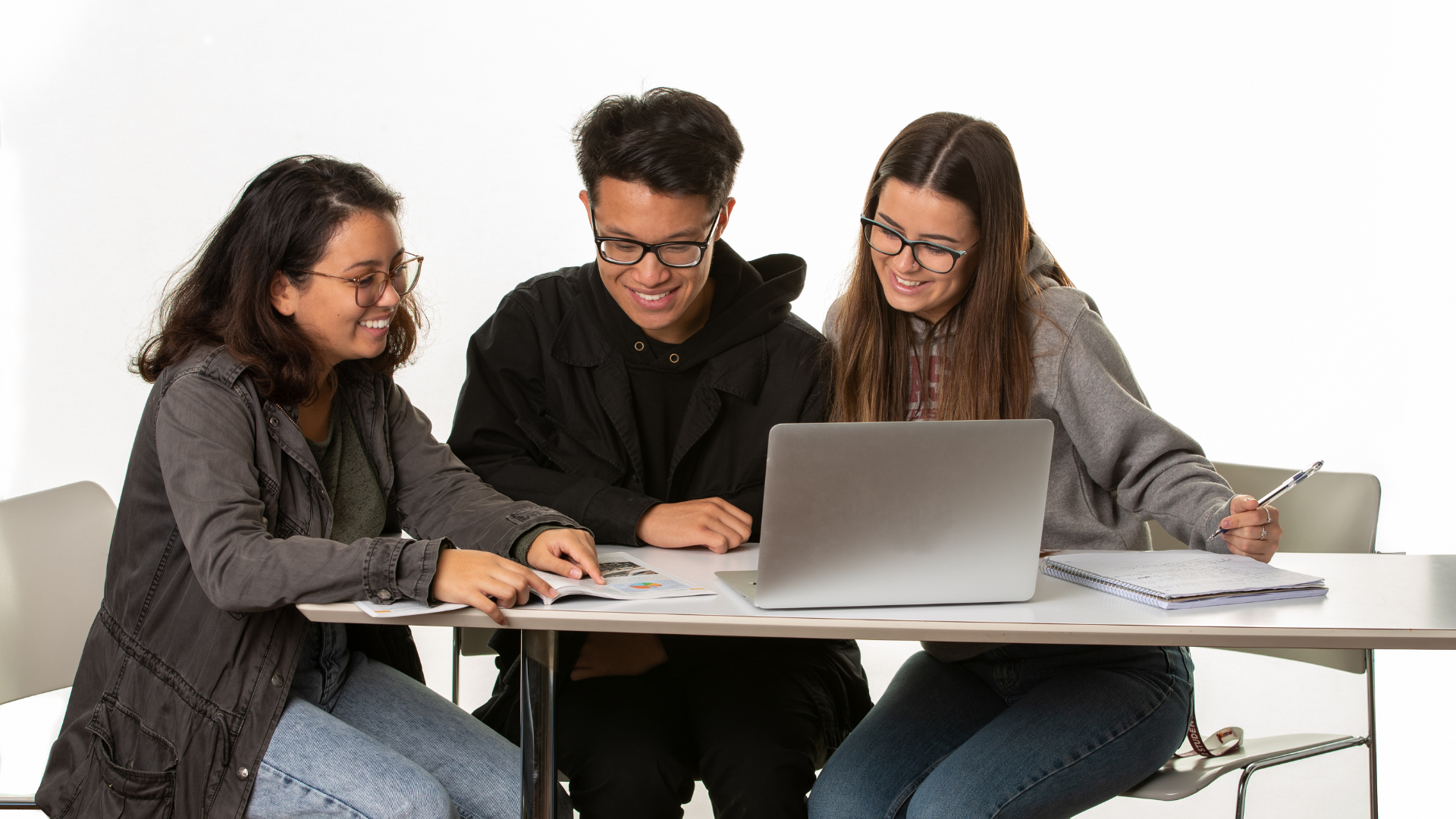 Three students gather at a desk, looking at a marketing report together.