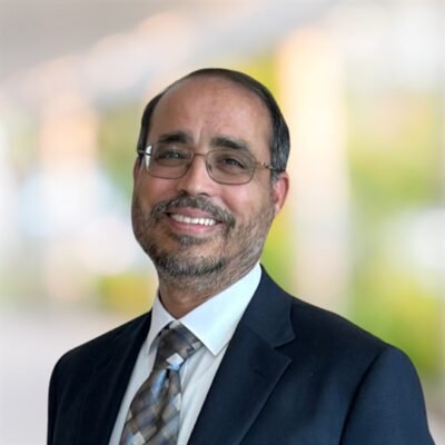 Headshot of Elkafi Hassini, smiling man with a blue suit and glasses